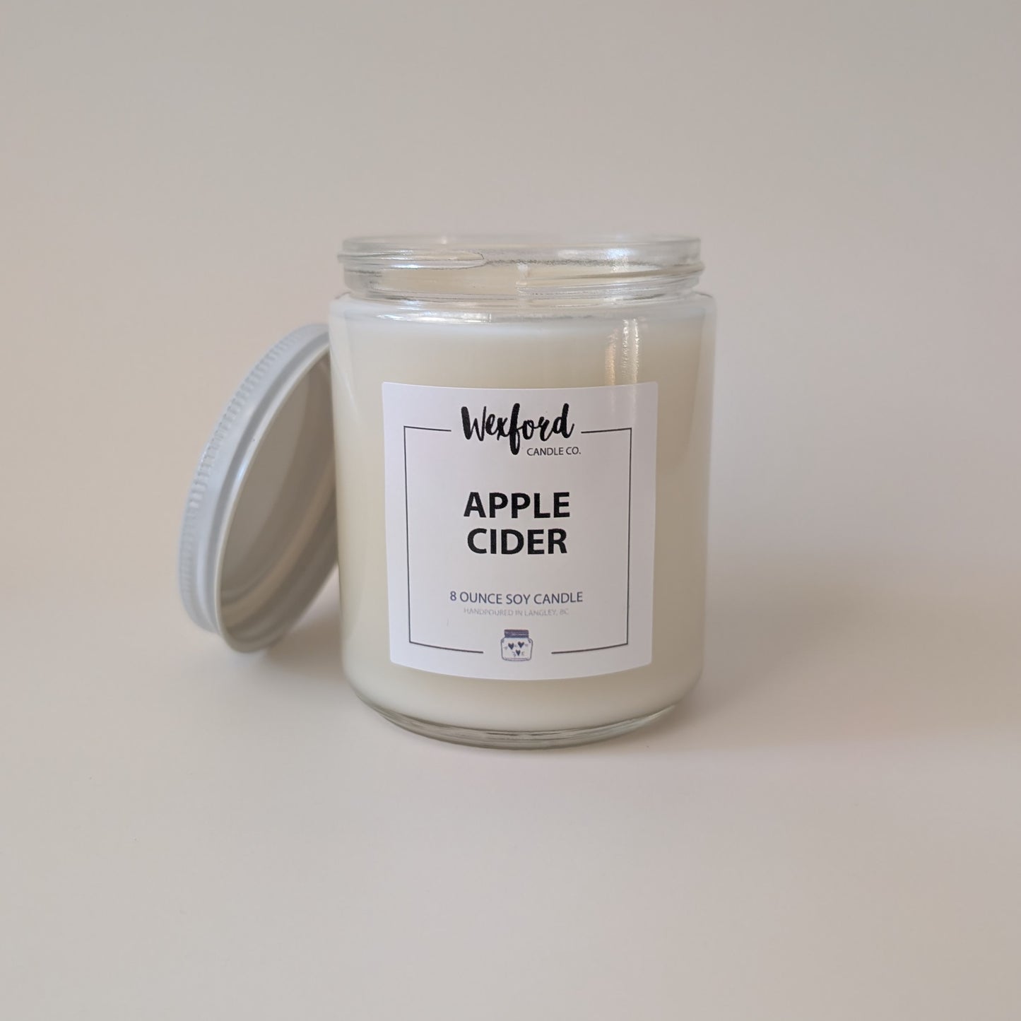 An 8 ounce soy candle in a clear glass jar with a white wax fill and a white label reading 'Wexford Candle Co. APPLE CIDER'.